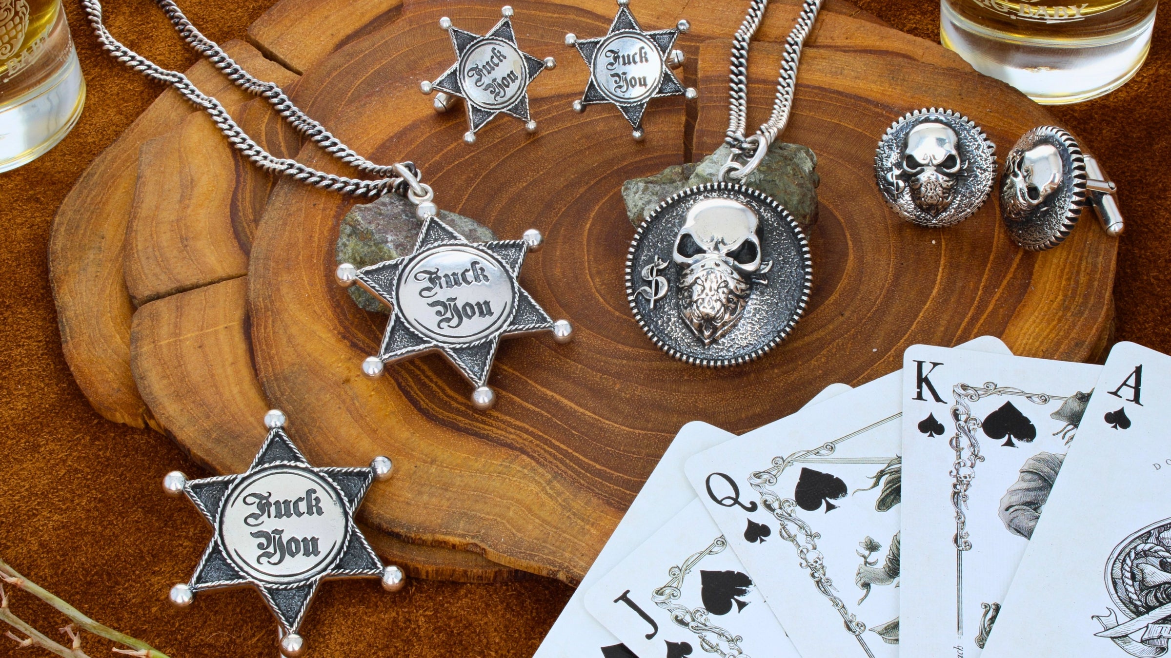 Silver jewelry with star designs and skull details on a wooden surface with playing cards.
