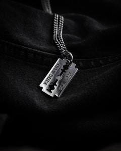 Style shot of razor blade pendant on chain on black denim background