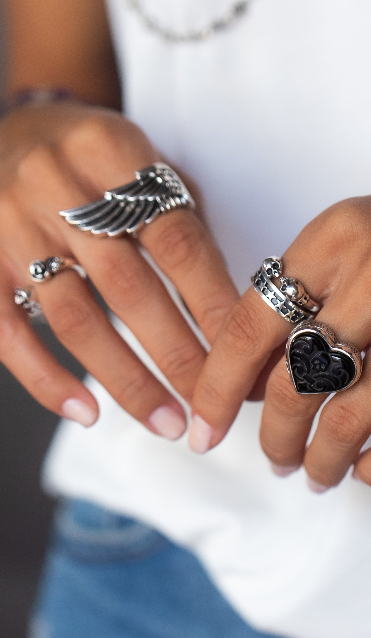 Close up shot of woman's hands with wing ring, black heart ring, skull ring and star ring.