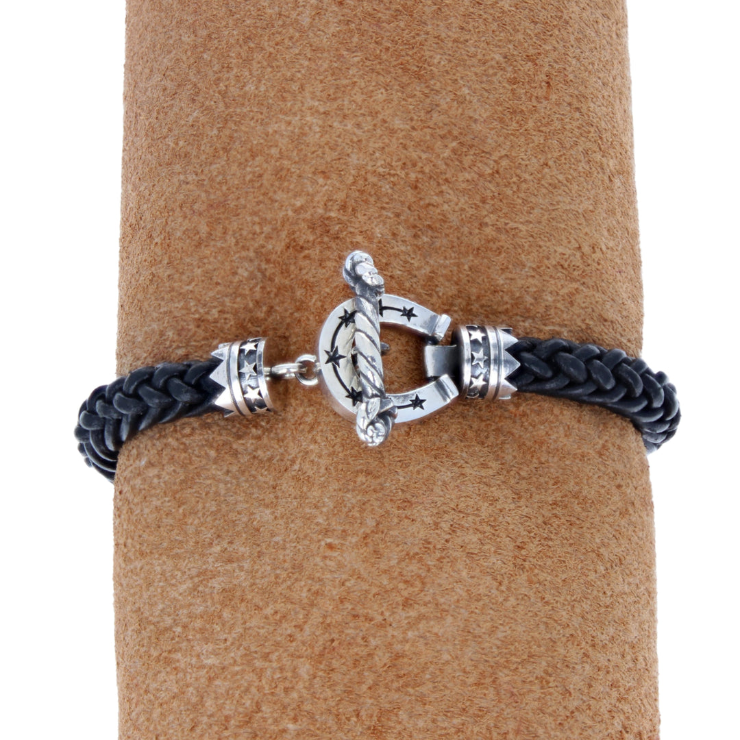 Bracelet with silver clasp and black cord on a brown cylindrical stand