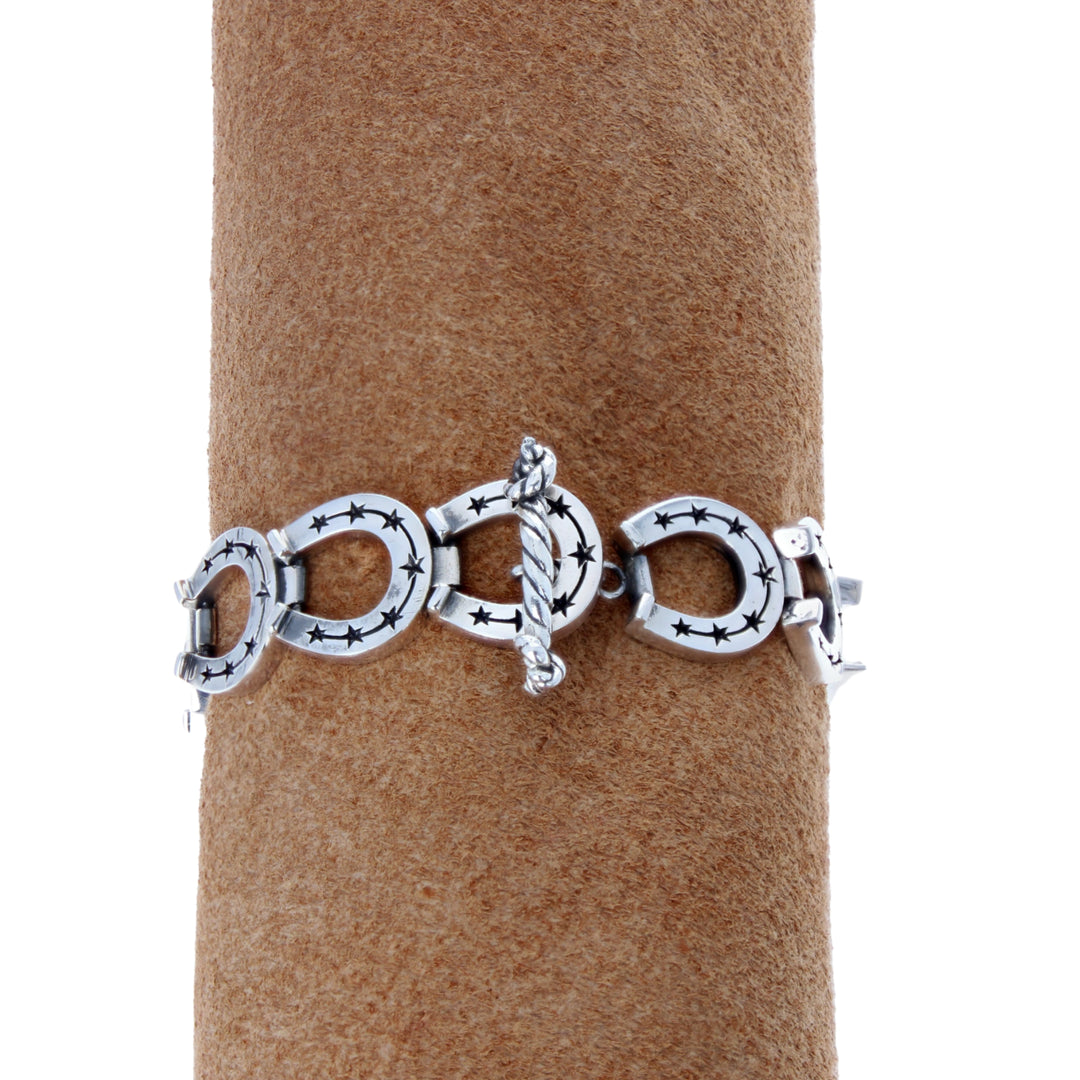 Silver bracelet with horseshoe designs on a brown cylindrical stand