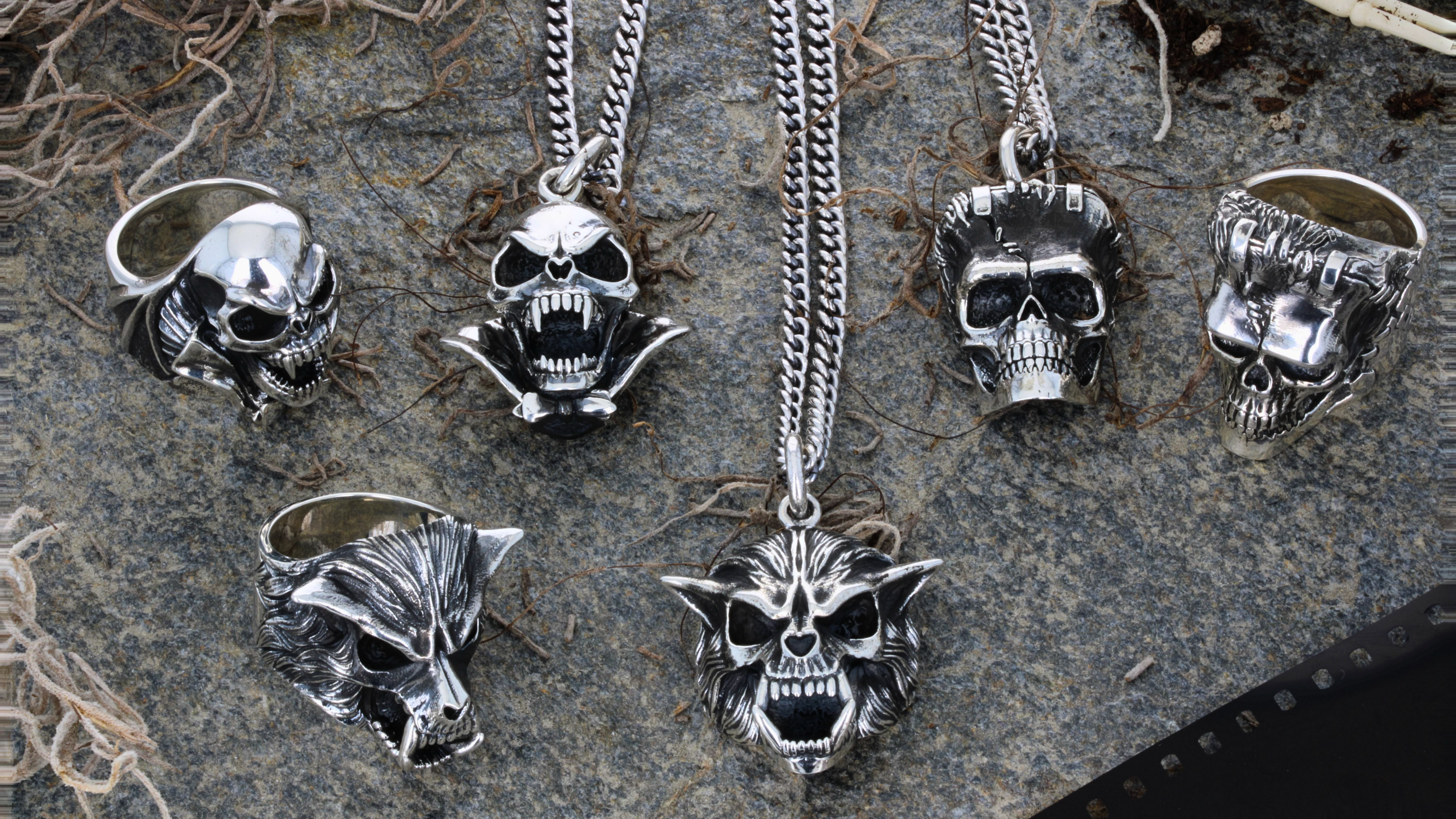 Collection of silver skull-themed jewelry including rings and pendants on a textured surface.