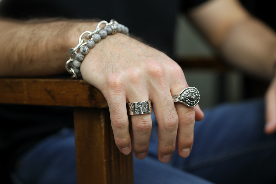 Hand wearing silver rings and bracelet on a wooden surface